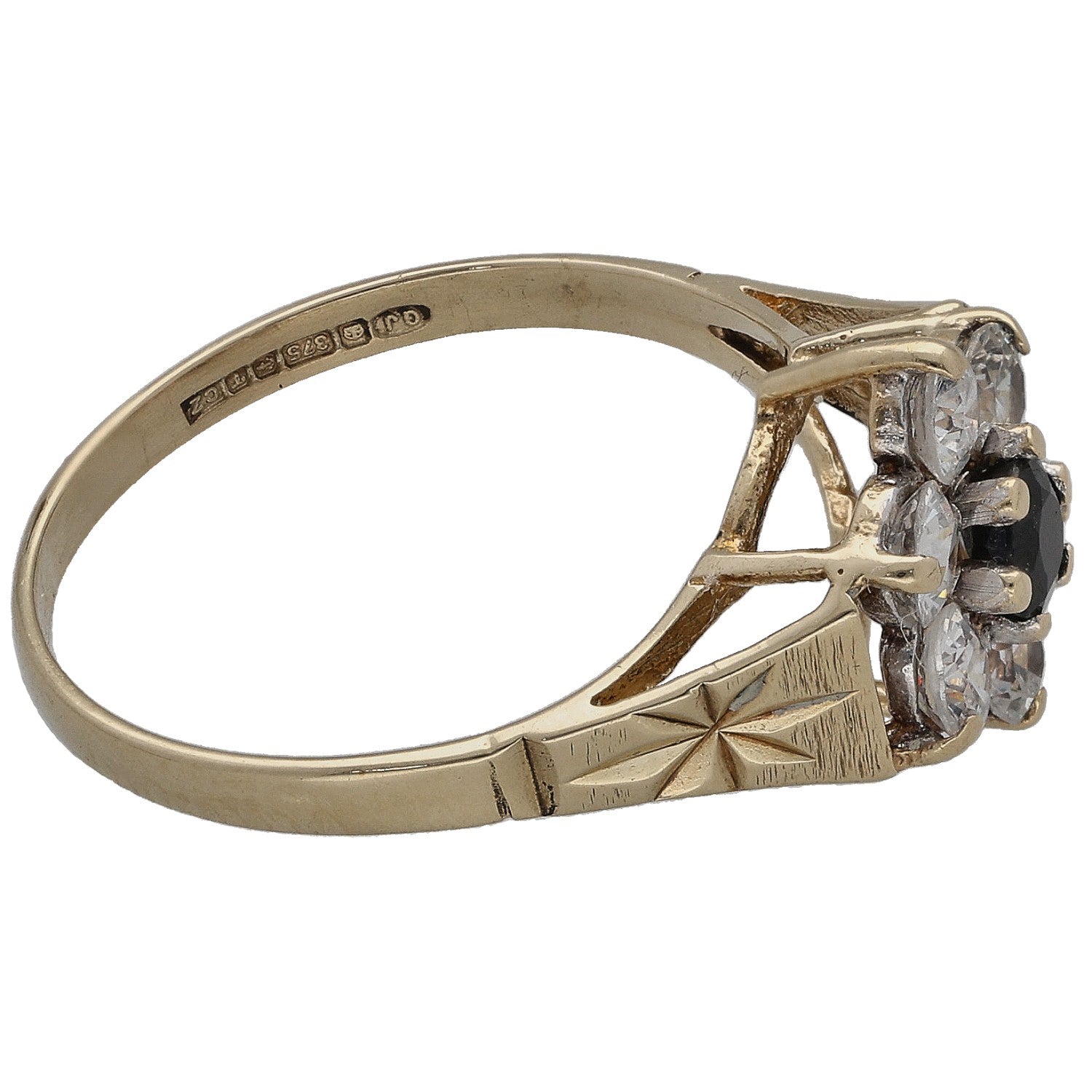 Gold tone ring side view with clear stones set around a dark center, geometric band engravings.