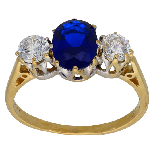 Gold three-stone ring with deep blue center stone and two clear round stones, openwork setting