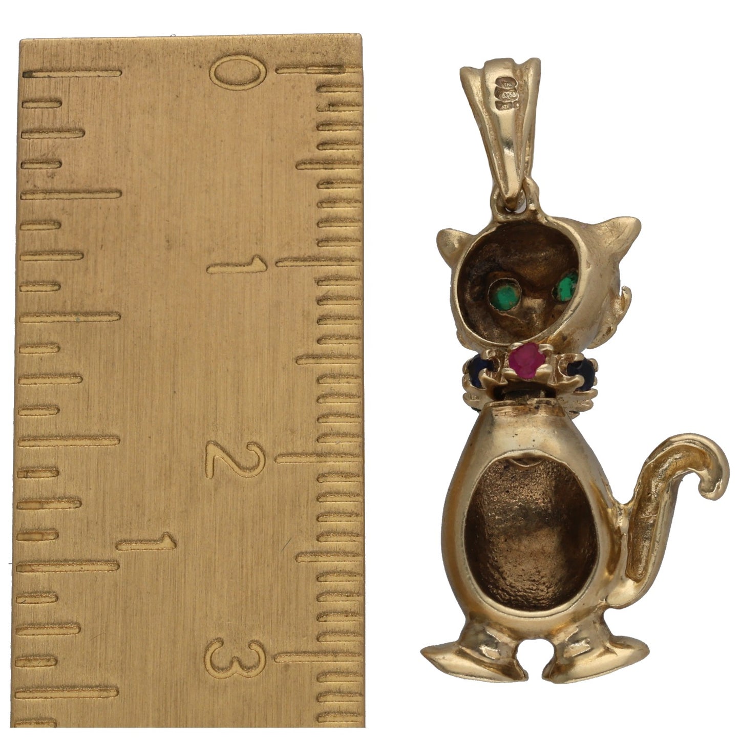 Gold cat pendant with green gemstone eyes and red/blue stones, side view on ruler
