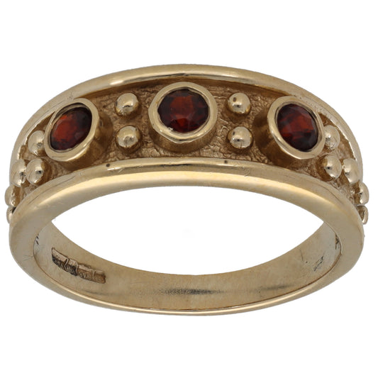 Three-stone gold ring with red garnet gemstones in bezel settings